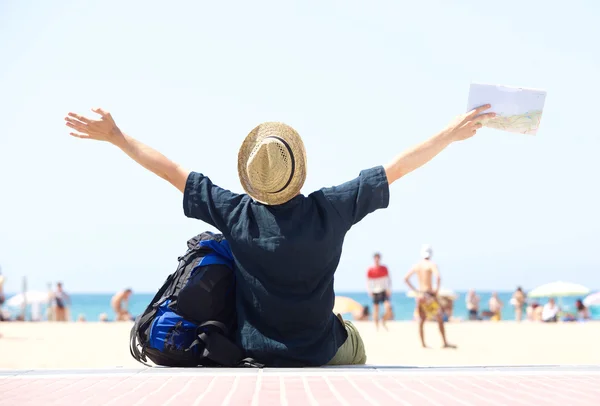 Travel man sitting by beach with arms outstretched — Stock Photo, Image