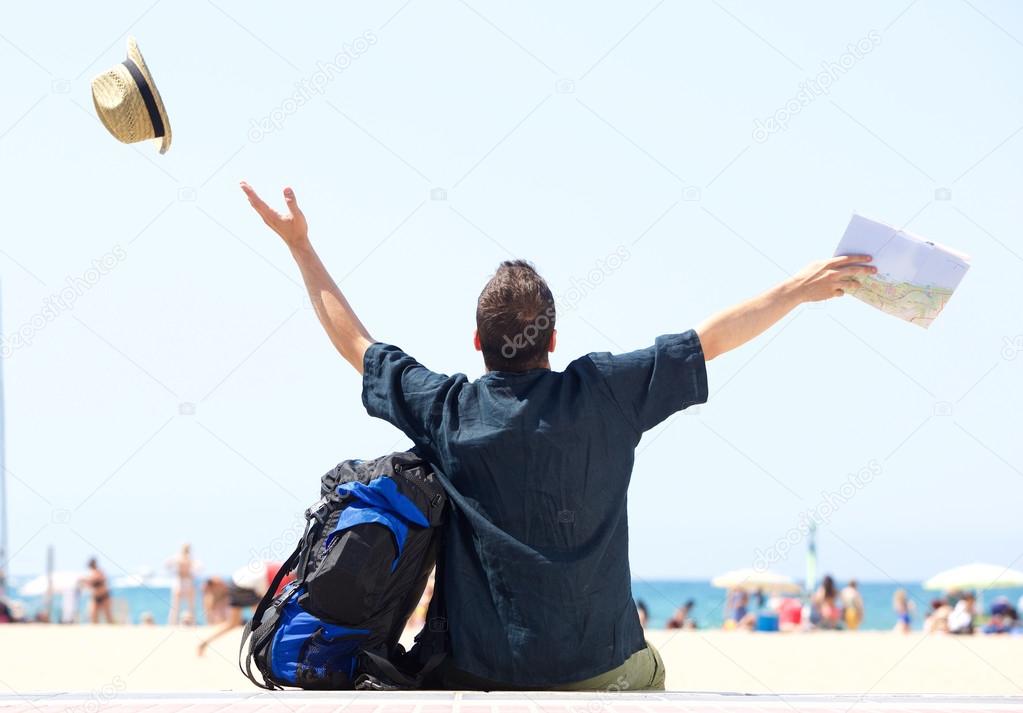 Happy man with bag and map arrives at beach