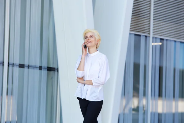 Wanita bisnis muda yang bahagia berjalan dan berbicara di telepon genggam — Stok Foto
