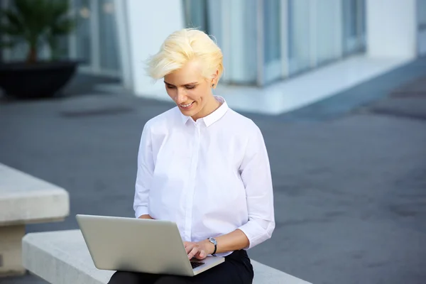 Sorridente giovane donna seduta fuori con il computer portatile — Foto Stock