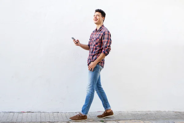 Glimlachende man lopen en luisteren naar muziek op mobiele telefoon — Stockfoto