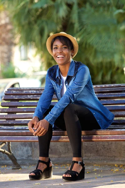 Sonriente joven negra sentada en el banco del parque — Foto de Stock