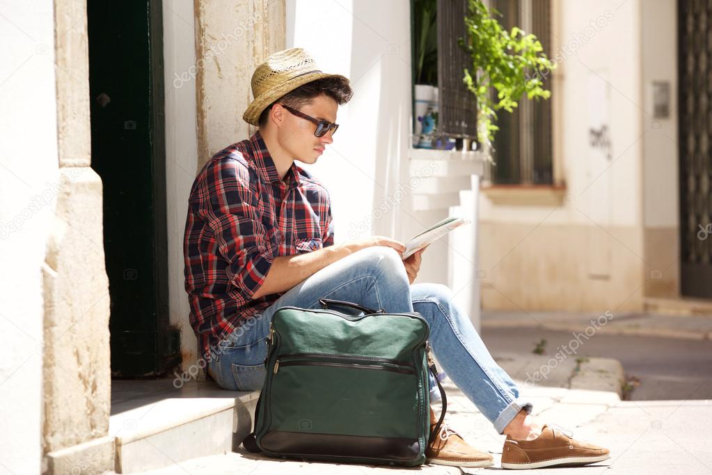 Traveling man sitting on sidewalk reading map