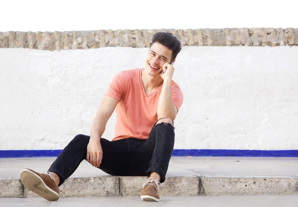 Smiling man sitting outside and listening to mobile phone — Stock Photo, Image