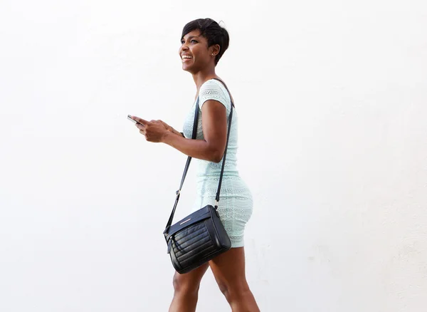 バッグや携帯電話と一緒に歩いている若い女性の笑みを浮かべてください。 — ストック写真