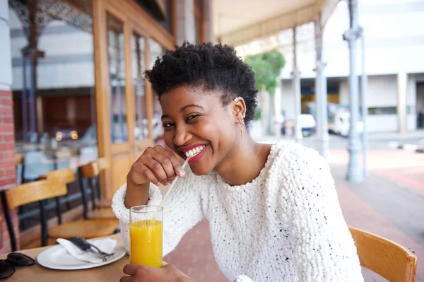 Sonriente chica negra bebiendo jugo de naranja en la cafetería al aire libre —  Fotos de Stock