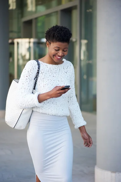 Усміхнена чорна жінка виходить на вулицю з мобільним телефоном — стокове фото