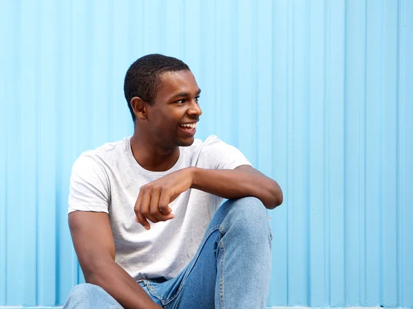 Улыбающийся африканский американец, сидящий на синем фоне — стоковое фото