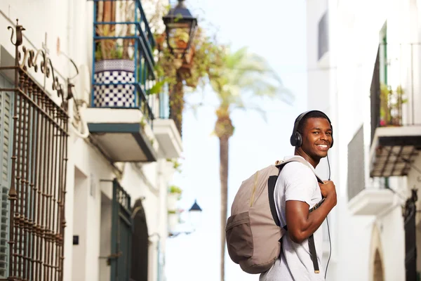 Uśmiechnięty mężczyzna Afrykanin podróżować z torba na słuchanie muzyki — Zdjęcie stockowe