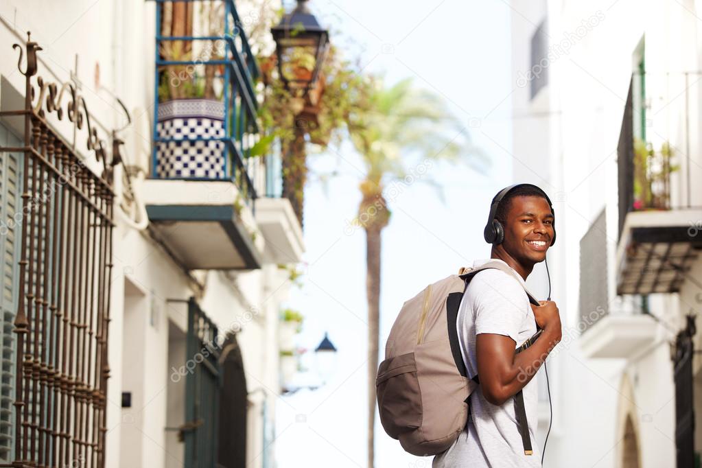 Smiling african travel man with bag listening to music