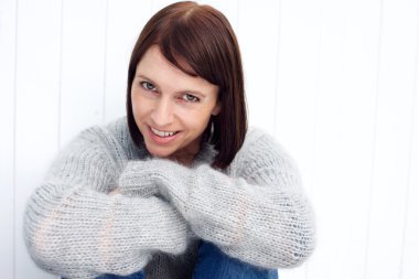 Gülümseyen orta yaşlı beyaz duvara oturan kadın