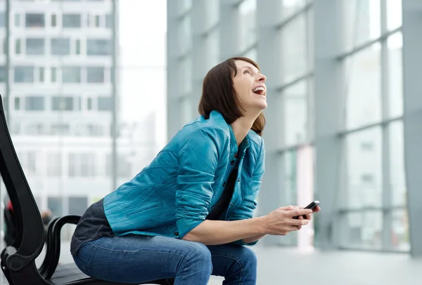 Laughing older woman sitting with mobile phone