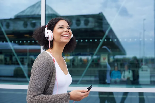 Jeune femme souriante marchant avec un téléphone portable et un casque — Photo