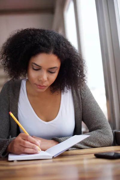 Jonge Afrikaanse Amerikaanse vrouwelijke student in boek schrijven — Stockfoto