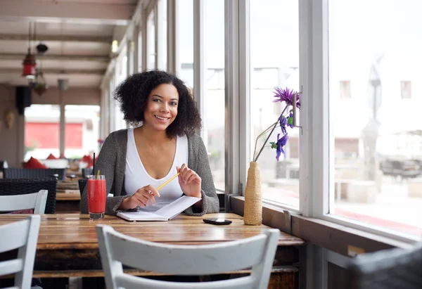 Smiling female college student sitting at cafe with pencil and book — Stock Photo, Image