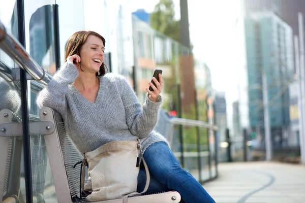 Starší žena s úsměvem a při pohledu na mobilní telefon — Stock fotografie