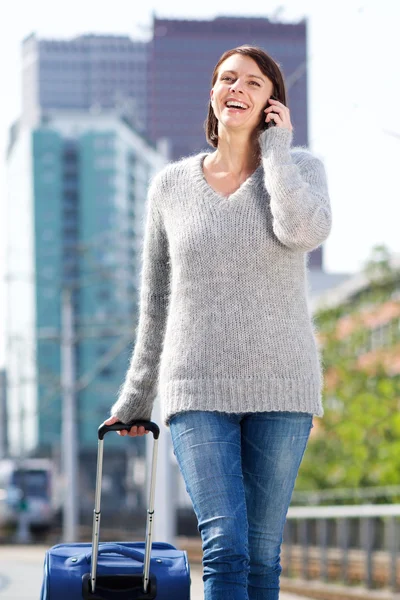 Smiling woman walking and talking on mobile phone with suitcase — Stock Photo, Image