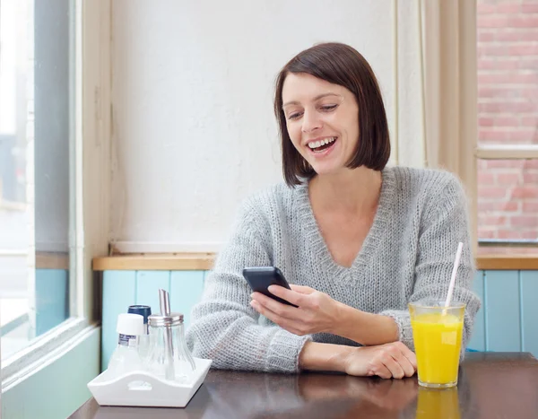 Привлекательная пожилая женщина улыбается на мобильный телефон в кафе — стоковое фото