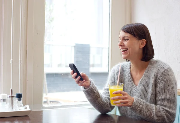 Сміється жінка сидить у кафе з мобільним телефоном — стокове фото