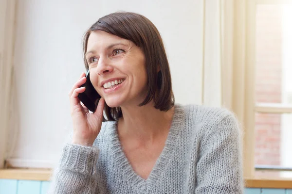 Attraktiv kvinna leende med mobiltelefonen hemma — Stockfoto