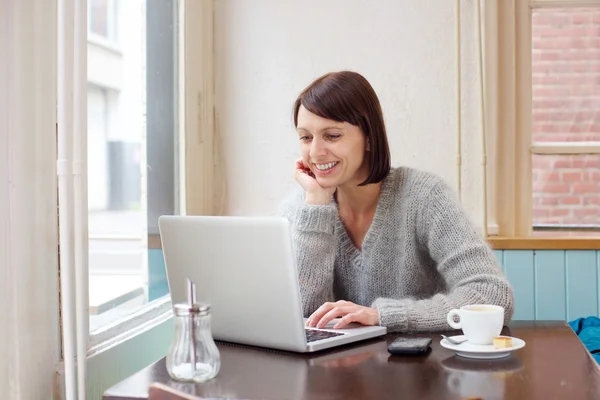 Gülümseyen laptop ile kafede oturan kadın — Stok fotoğraf