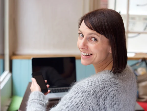 Mujer sonriente con teléfono móvil y ordenador portátil en casa —  Fotos de Stock