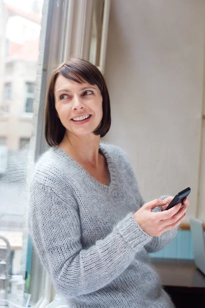 Usměvavá starší žena doma pomocí mobilního telefonu — Stock fotografie