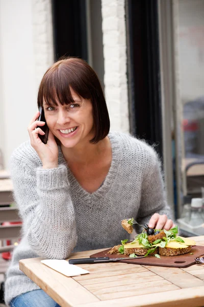 Žena jí a usmíval se s mobilním telefonem — Stock fotografie