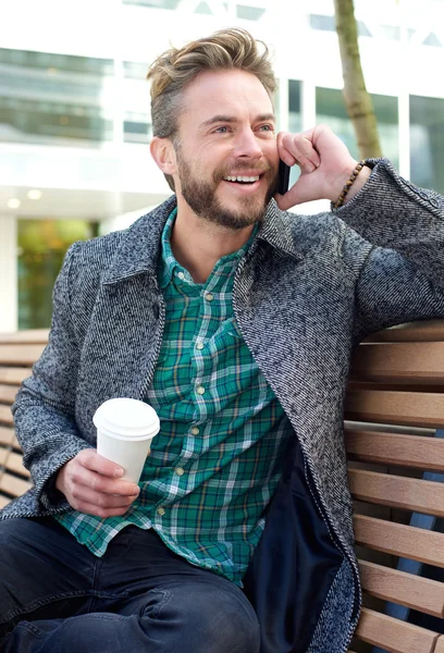 Lächelnder Mann sitzt draußen mit Handy — Stockfoto