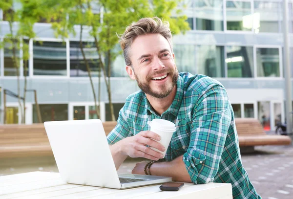 Hombre guapo sentado al aire libre con ordenador portátil y café —  Fotos de Stock