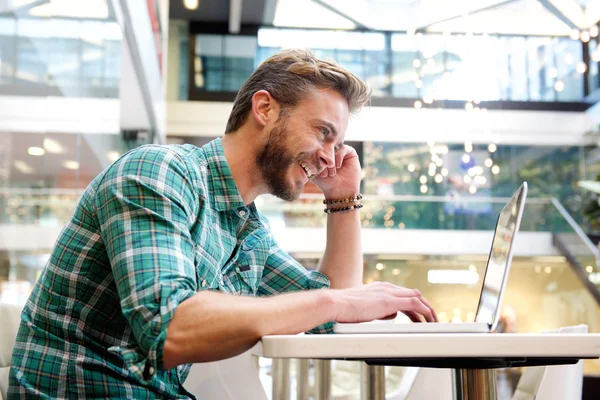 Hombre atractivo sonriendo con portátil en el centro comercial —  Fotos de Stock