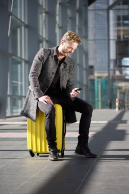 Cep telefonu görünümlü çanta üzerinde oturan serin seyahat adam