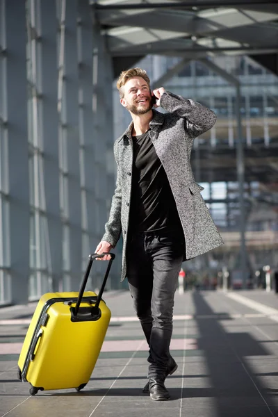 Uomo da viaggio sorridente che cammina con cellulare e valigia — Foto Stock