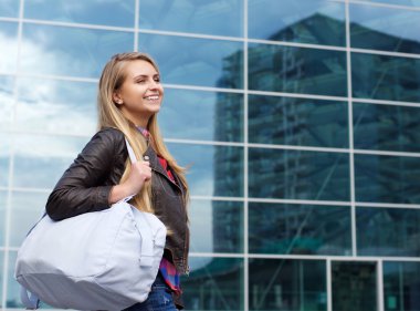 Gülümseyen genç kadın çantası ile şehirde yürüyüş