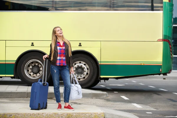 Усміхнена подорожня жінка стоїть на автобусному терміналі з сумками — стокове фото