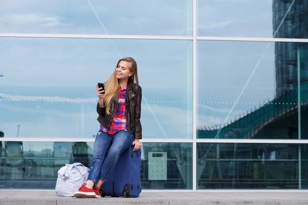 Joven mujer viajera sentada en una maleta mirando el teléfono móvil —  Fotos de Stock