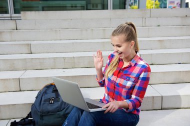 Gülümseyen öğrenci dizüstü sallayarak dışında oturan
