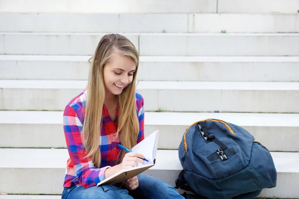 Souriante fille assise dehors écrivant dans le livre — Photo