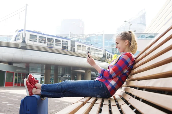 Mujer sonriente de viaje sentada afuera con teléfono móvil — Foto de Stock