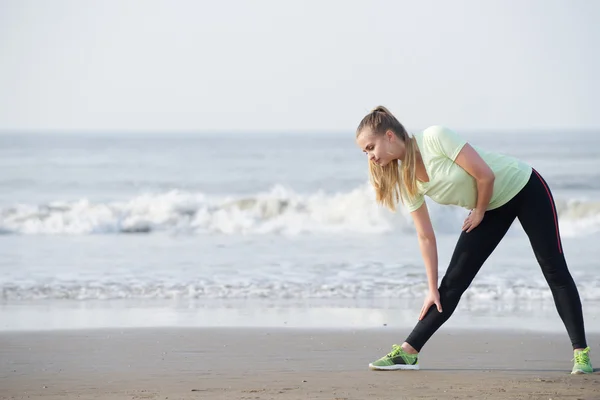 Sportowy młoda kobieta schylania się rozciąganie na plaży — Zdjęcie stockowe