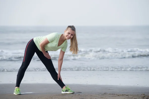Usmívající se sportovní žena táhnoucí se na pláži — Stock fotografie