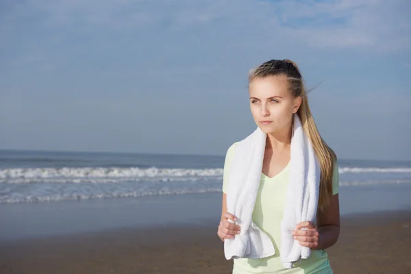 Fitness mladá žena stojí na pláži s ručníkem — Stock fotografie