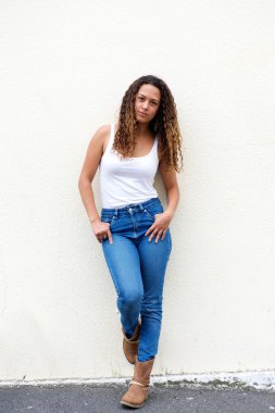 Genç kadın bir duvara karşı ayakta kot pantolon