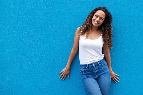 Портрет усміхненої молодої жінки, що стоїть на синій стіні — стокове фото