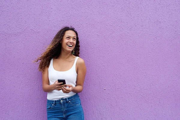 Улыбающаяся молодая женщина с мобильным телефоном смотрит в сторону — стоковое фото