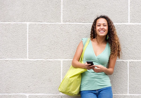 Mujer joven sonriente sosteniendo el teléfono móvil y la bolsa — Foto de Stock