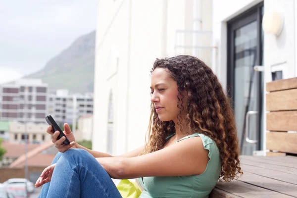 Mujer joven sentada afuera leyendo un mensaje de texto —  Fotos de Stock