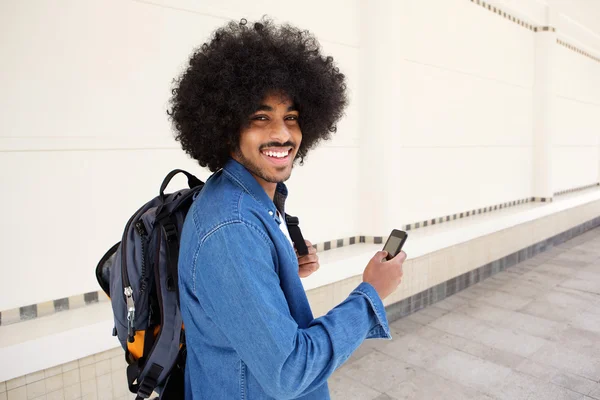 Joven hombre moderno sonriendo con bolsa y teléfono celular — Foto de Stock