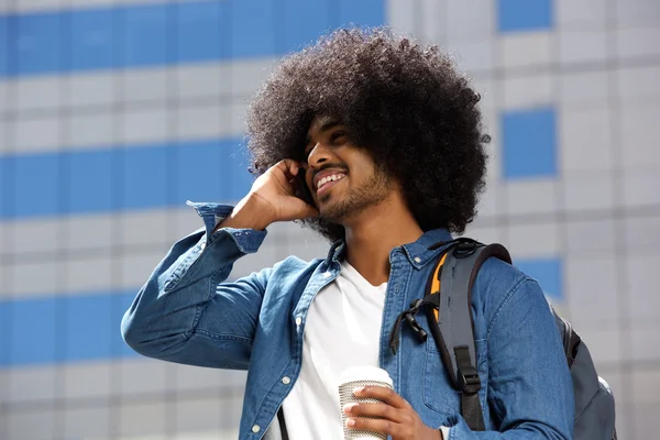 Улыбающийся черный мужчина с афро с помощью мобильного телефона в городе — стоковое фото