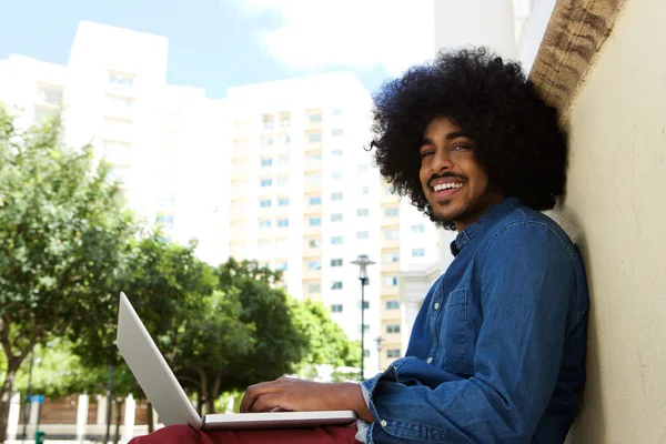 Hombre negro sonriente usando portátil en la ciudad —  Fotos de Stock